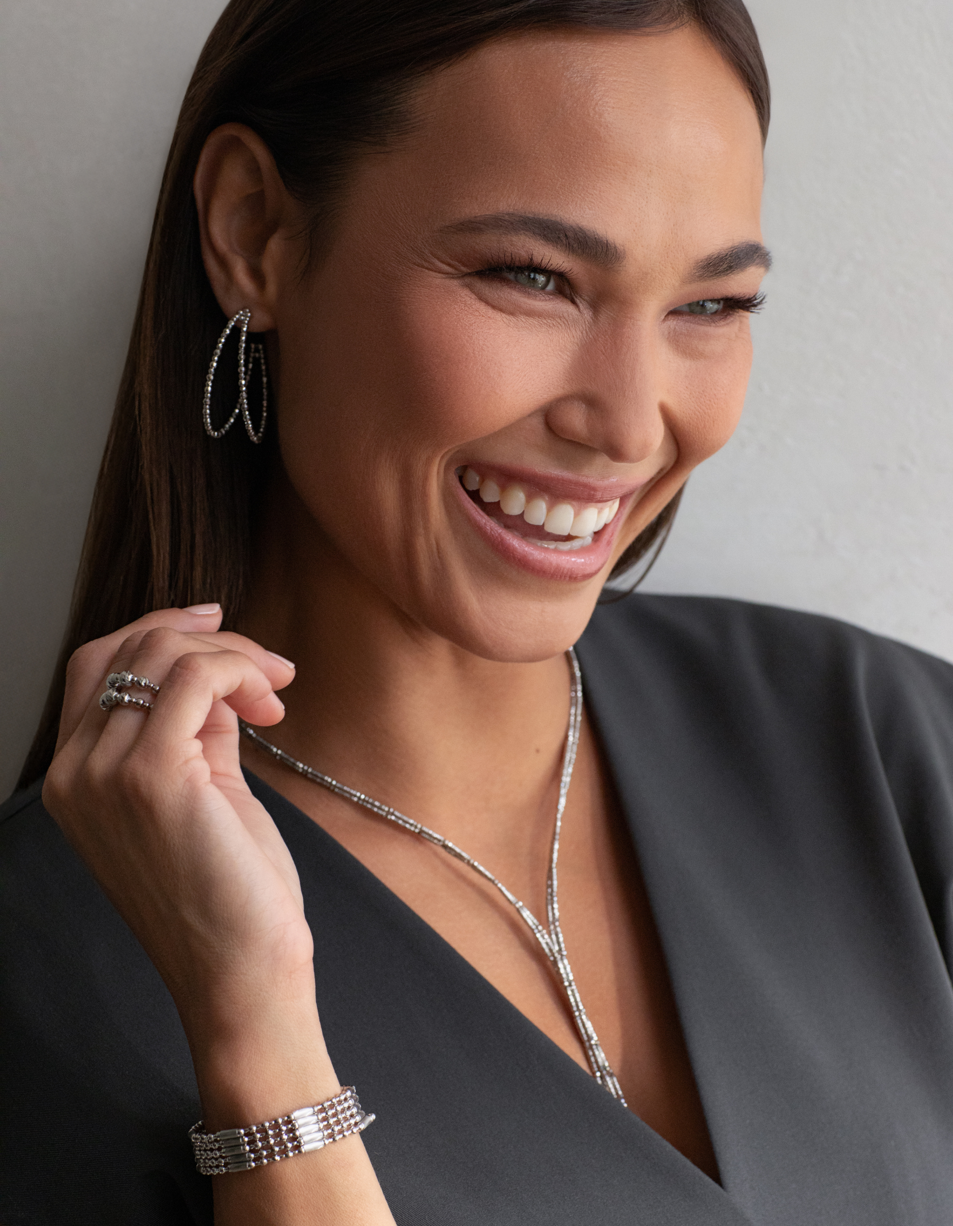 A model wearing a grey blazer with several Platinum Born jewelry pieces