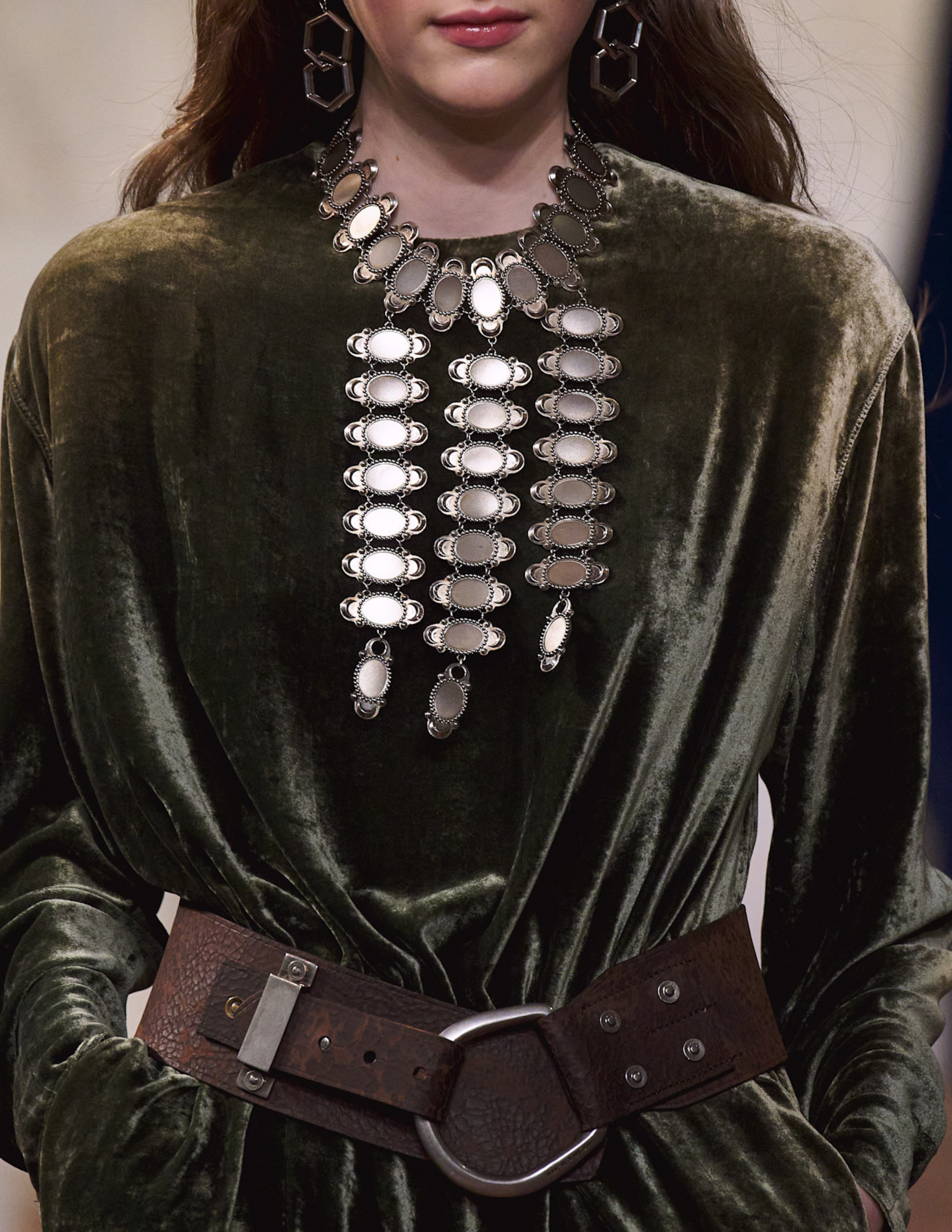 Ralph Lauren runway model wearing a waterfall coin necklace, green velvet dress, and a chunky brown belt.