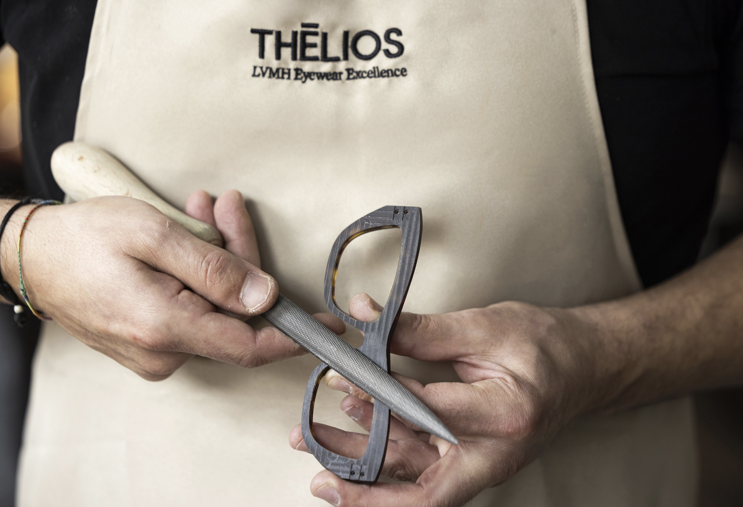 Thélios Eyewear being manufactured by a man wearing an apron that reads "Thélios: LVMH Eyewear Excellence"