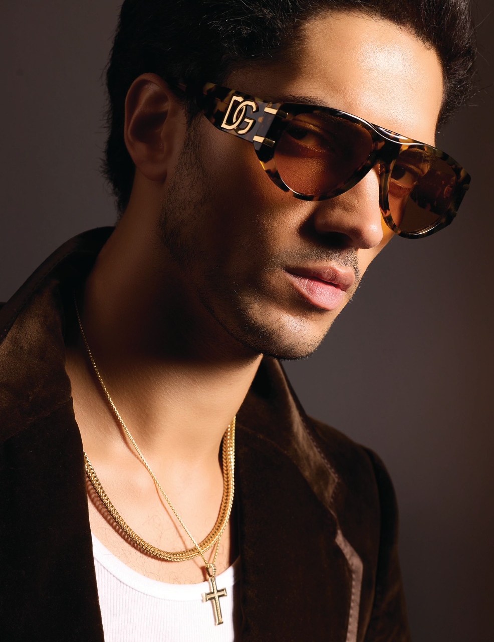 Waled wearing large Dolce & Gabnana sunglasses, a white tank top, gold chains and cross, with a brown velvet jacket