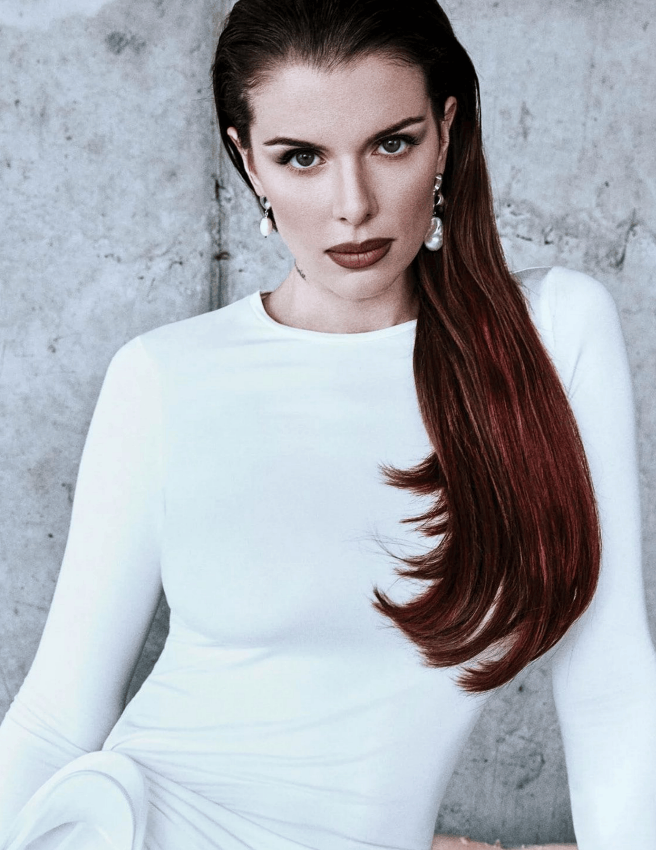 Studio portrait of Julia Fox in a fitted white dress with long dark red hair.