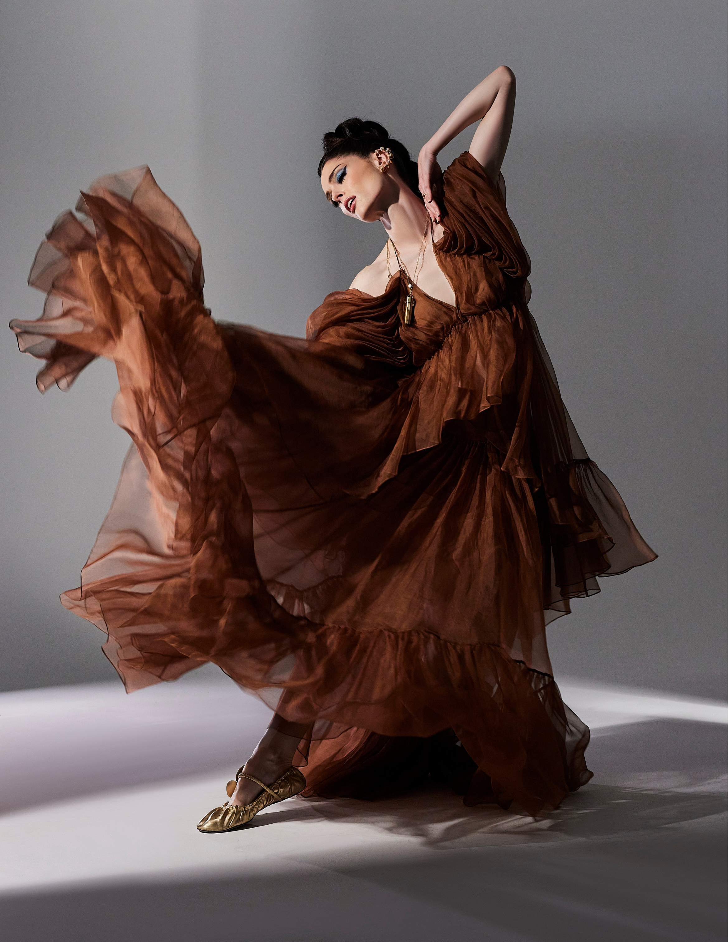 Fashion portrait of Coco Rocha wearing a flowing rust-colored couture gown captured in a dynamic dance-inspired pose