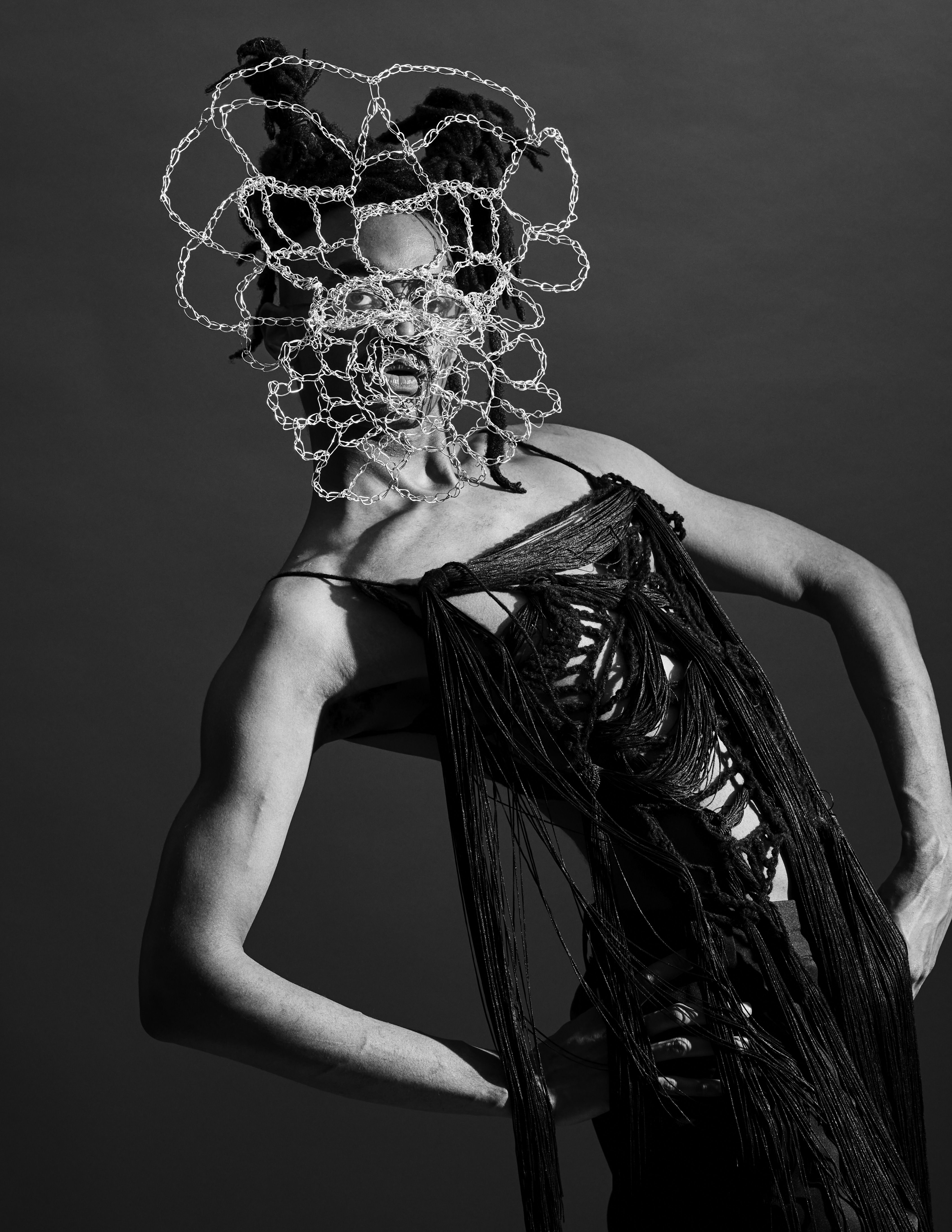 Jameel Mohammed, founder of Khiry, in a black & white photo wearing his own designs: an oversized intricate silver chain mask.
