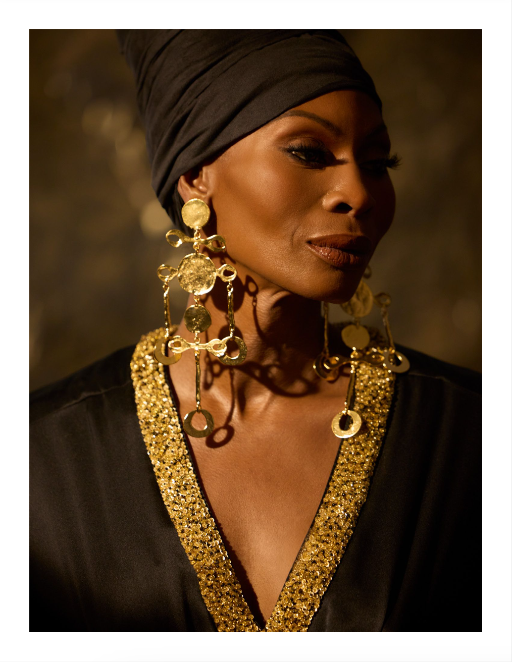 Dominique Jackson on a dramatic studio background with bold, chunky gold jewelry