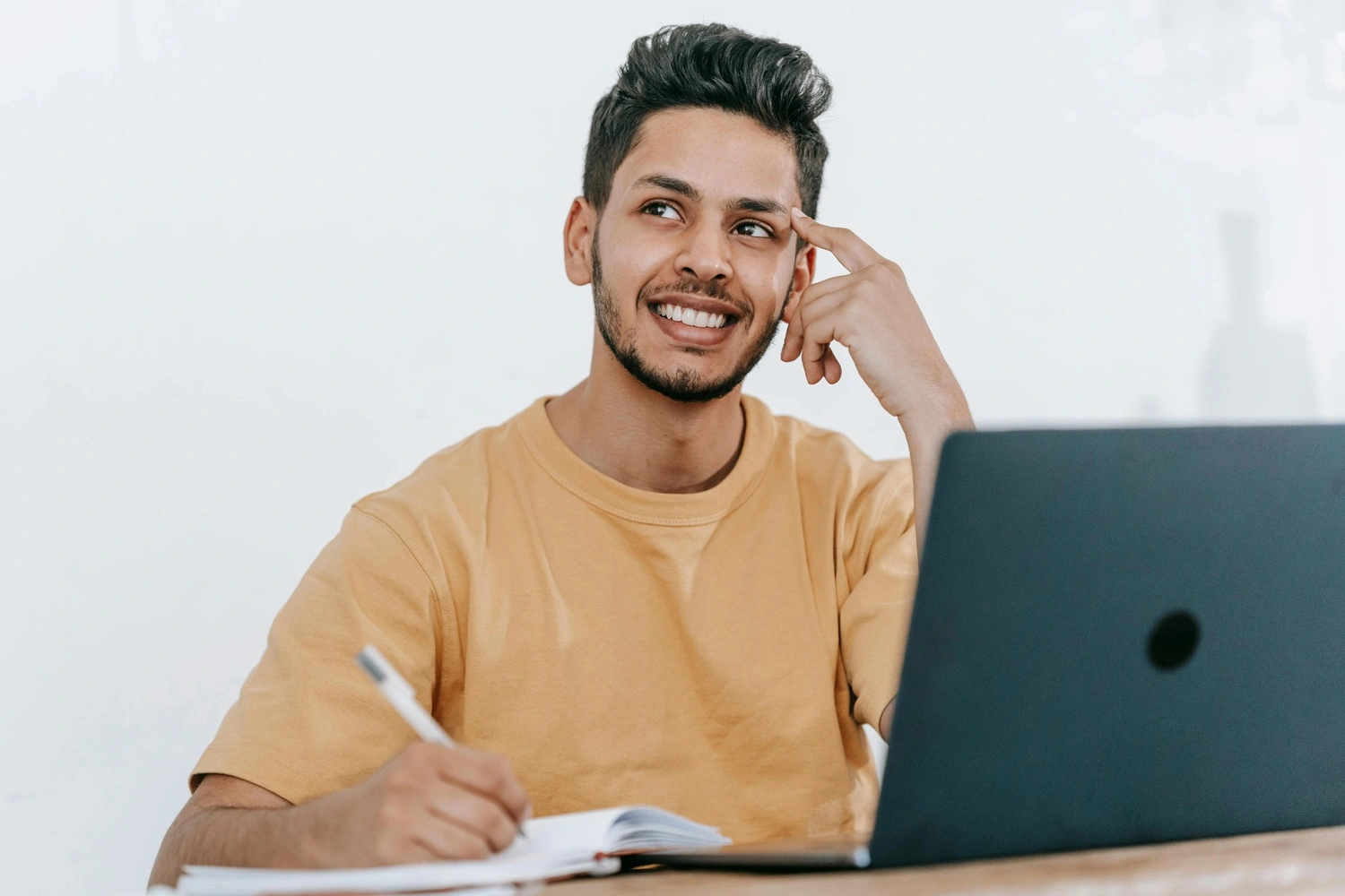 Man thoughtfully proofreading his essay, sitting at a desk with a notebook and laptop, representing essay proofreading services.
