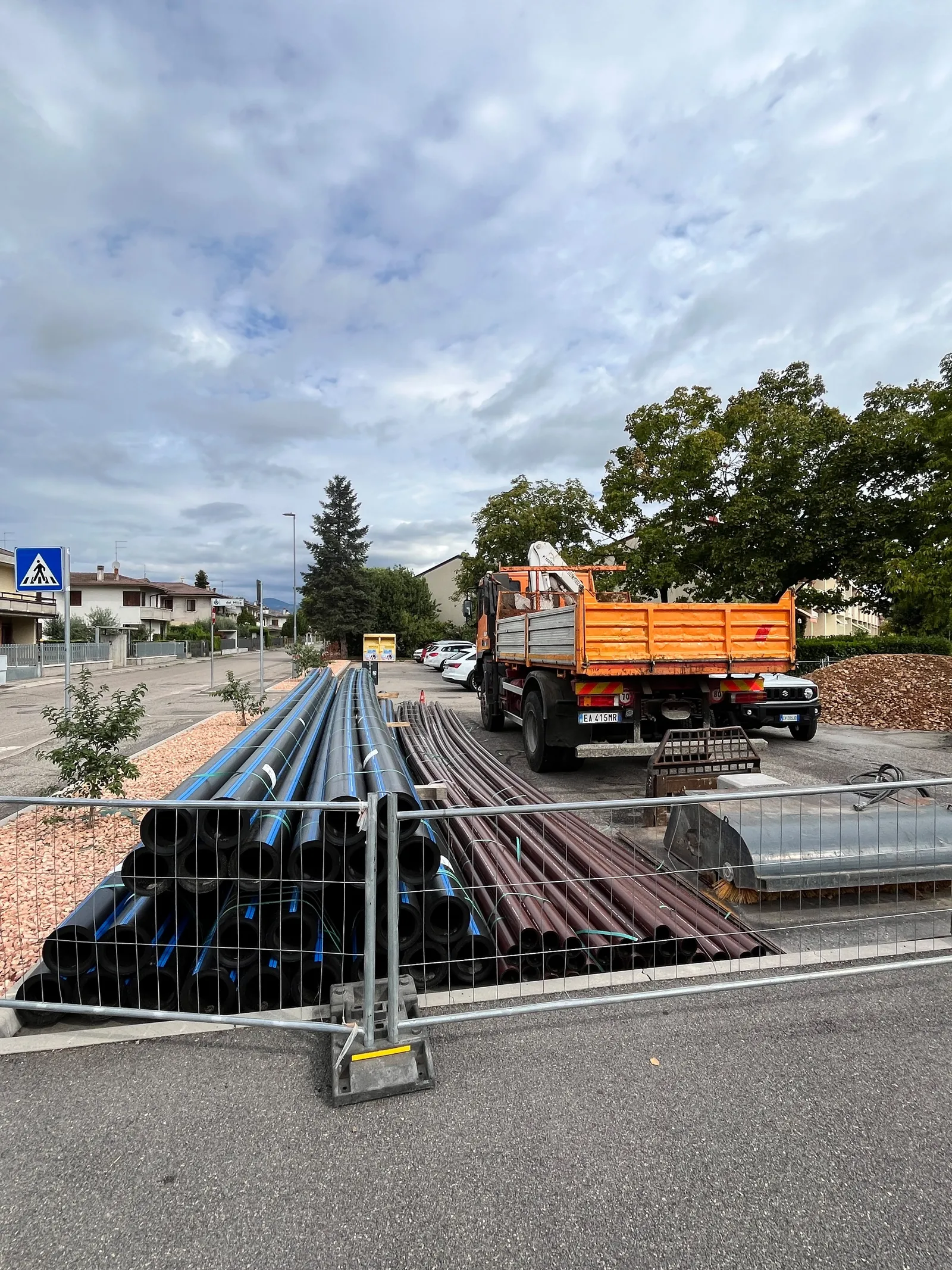 Cantieri stradali con tubature in plastica e un camion ribaltabile parcheggiati in un'area recintata.