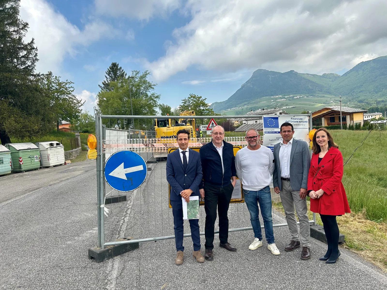 Un gruppo di persone posa davanti a un cantiere stradale finanziato dall'Unione Europea, con una montagna sullo sfondo.
