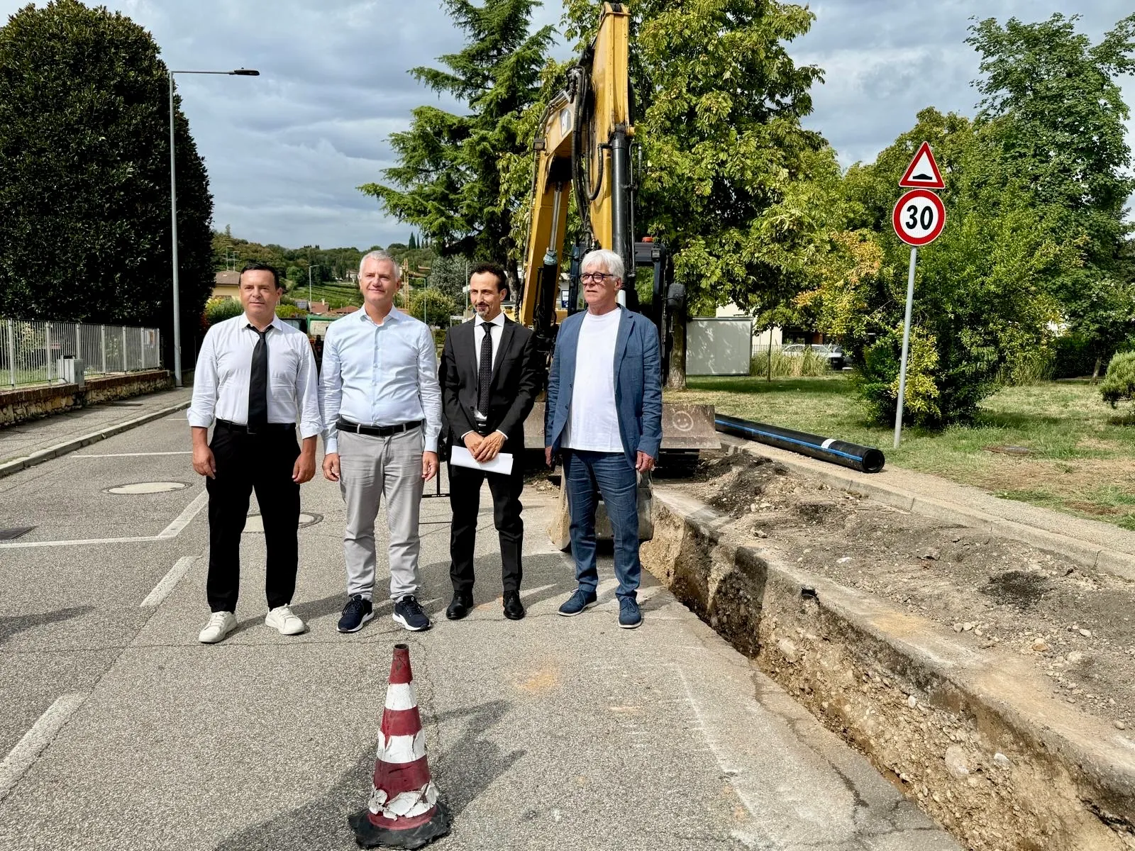 Sopralluogo tecnico ai lavori in corso: quattro uomini posano davanti a un escavatore in un cantiere stradale.