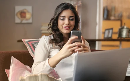 A woman on her phone in front of the computer