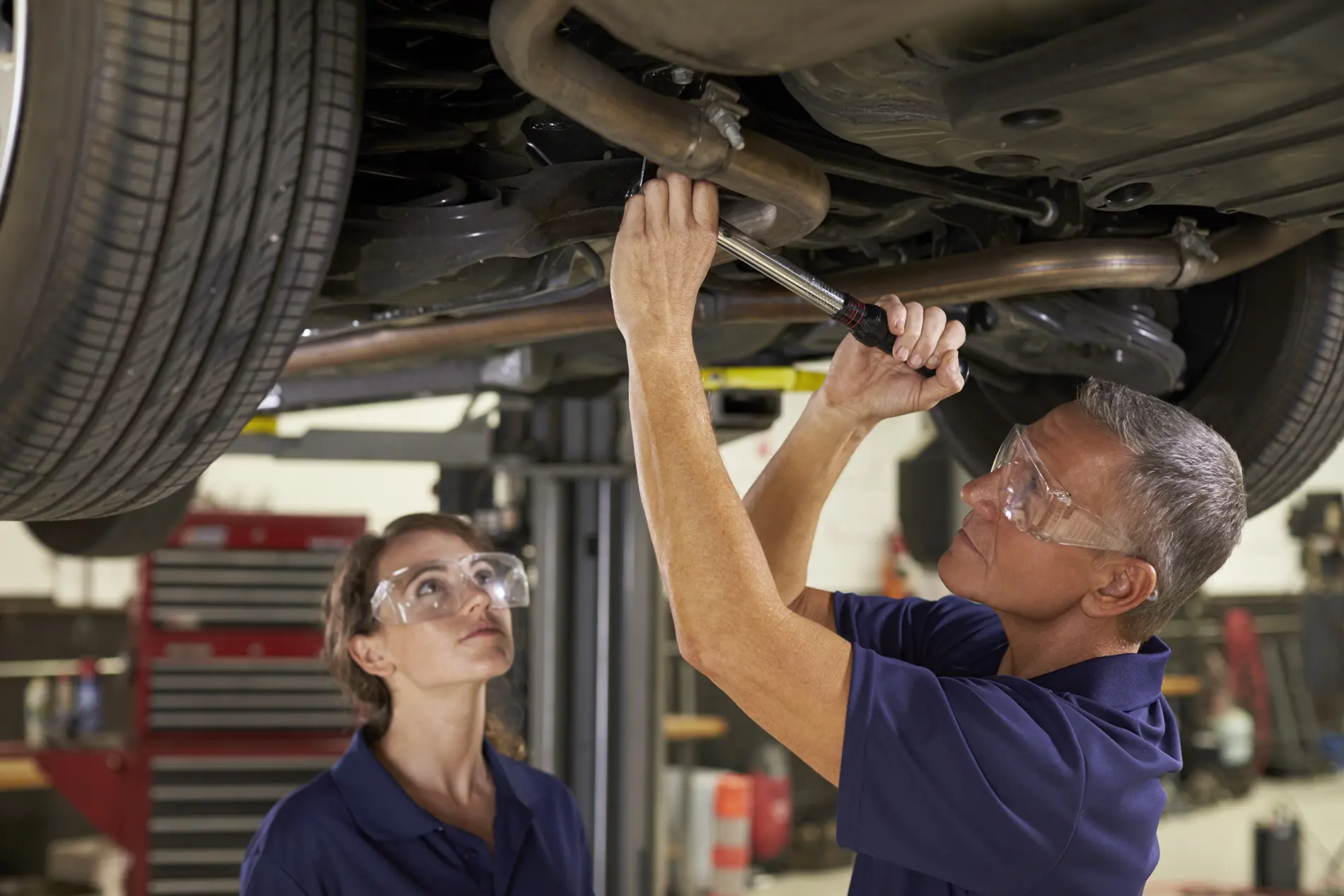 Male and Female Technicians Fixing an Exhaust under a vehicle