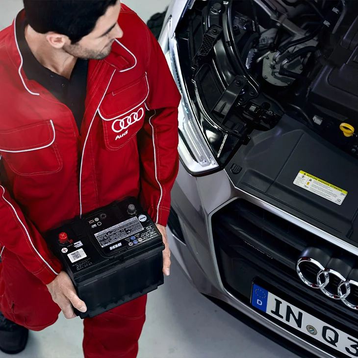 An audi technician carrying an Audi battery to replace it in an Audi vehicle