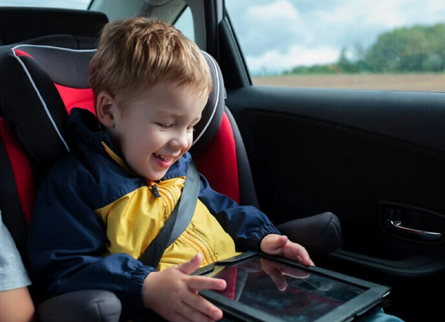 A child playing on a tablet in the back seat