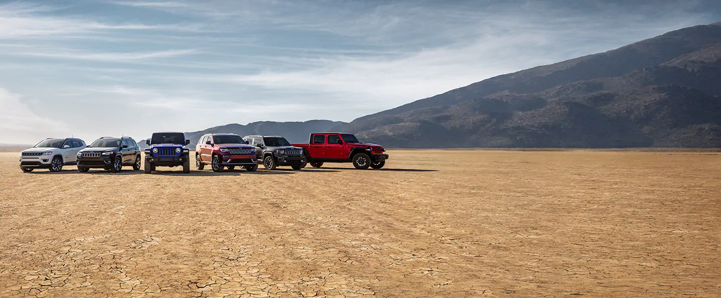 An image of several Jeeps lined up in a desert with a scenic view of a mountain range in the back.