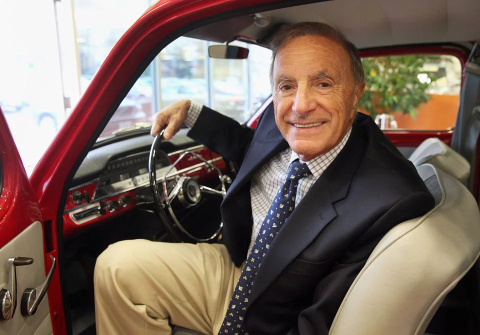 Ray Ciccolo sitting in an old red car with the door open looking a you and smiling