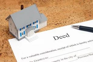 iniature house model beside a pen and a property deed document illustrating real estate ownership transfer and legal documentation services by AECORD.