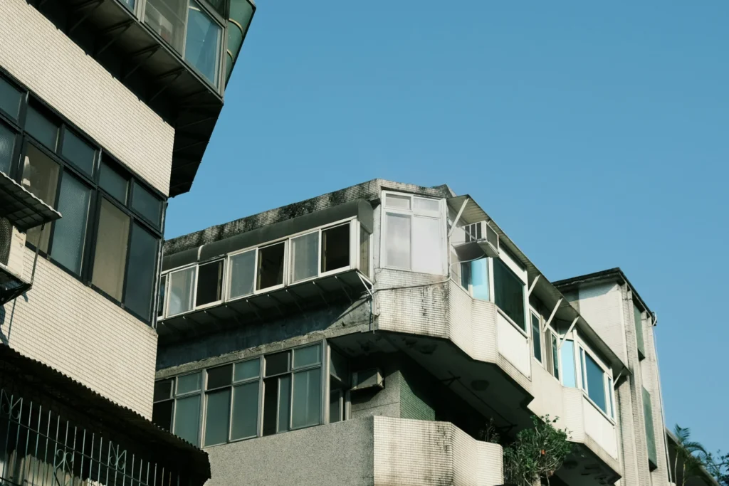 Aging mid-rise residential buildings with multiple windows and balconies against a blue sky, symbolizing urban projects that need local building plan sanctions and approval services from AECORD