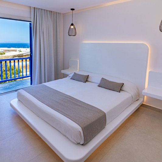 The interior of the room with the bed and the underlights, the modern bedside tables and a glimpse of the amazing view of the sea and the blue sky