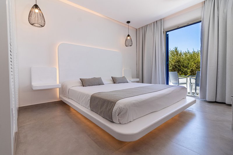 The interior of the room with the bed and the underlights, the modern bedside tables and a glimpse of the balcony and the sky