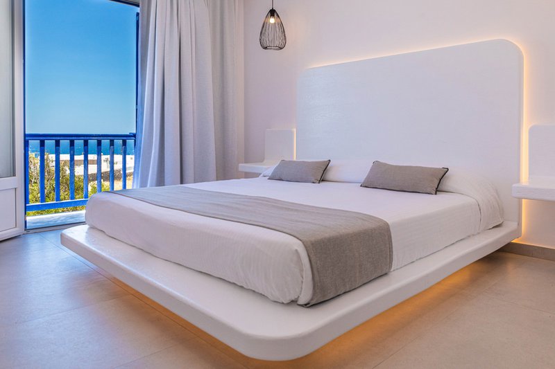 The interior of the room with the bed and the underlights, the modern bedside tables and a glimpse of the amazing view of the sea and the blue sky