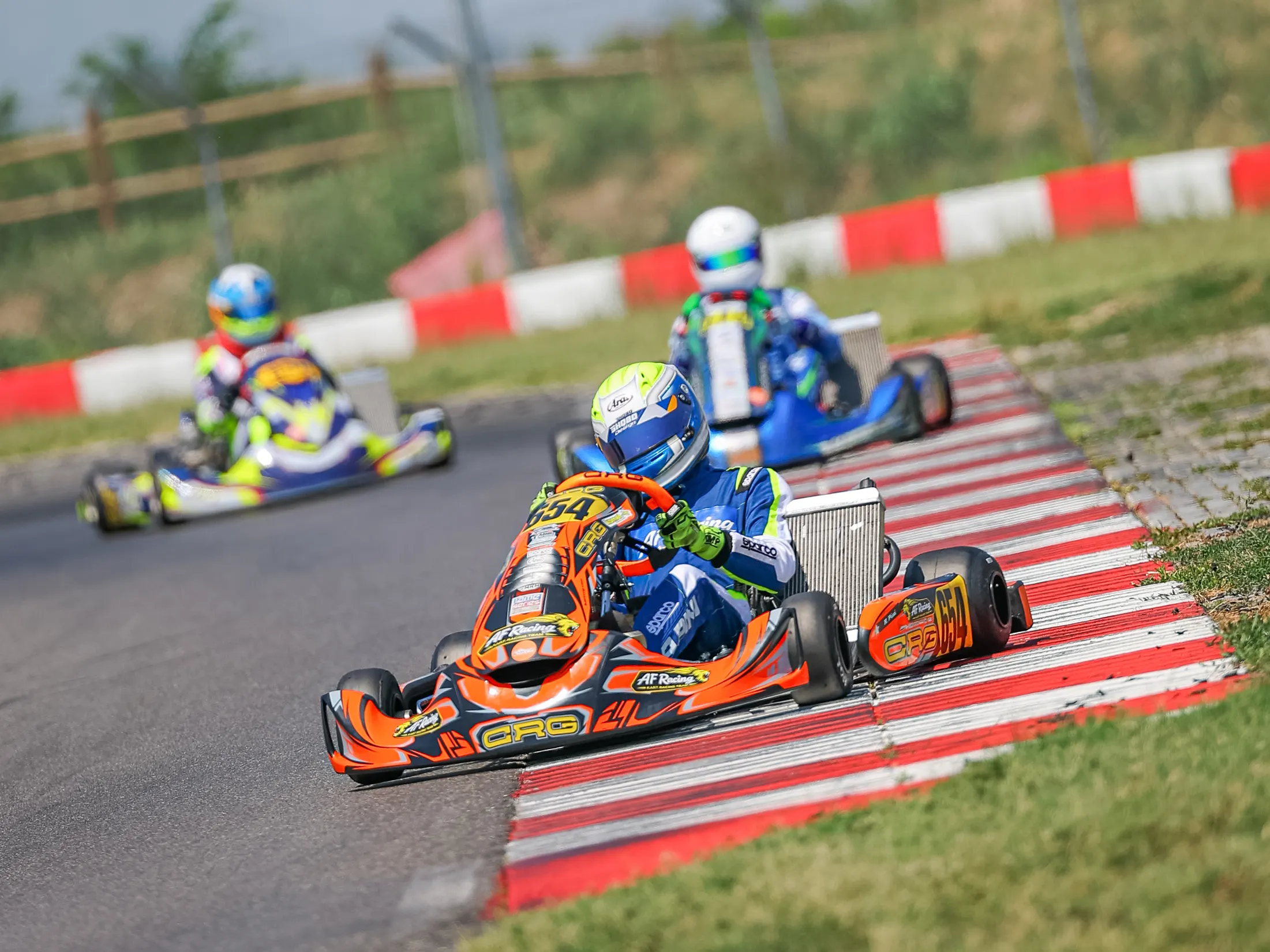 Kart arancione in testa a un gruppo sul cordolo bianco e rosso