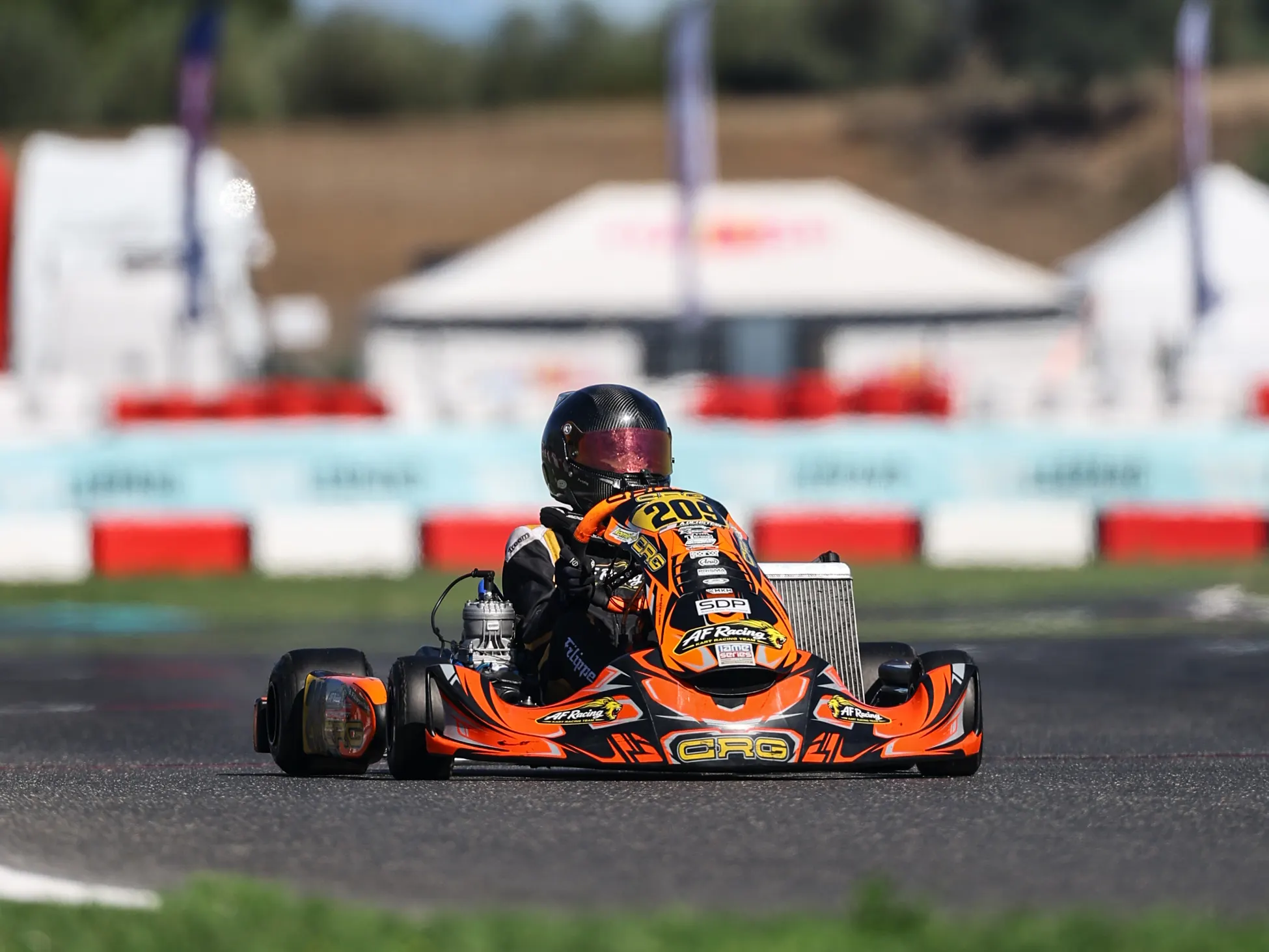 Kart arancione sul rettilineo davanti ai gazebo del paddock