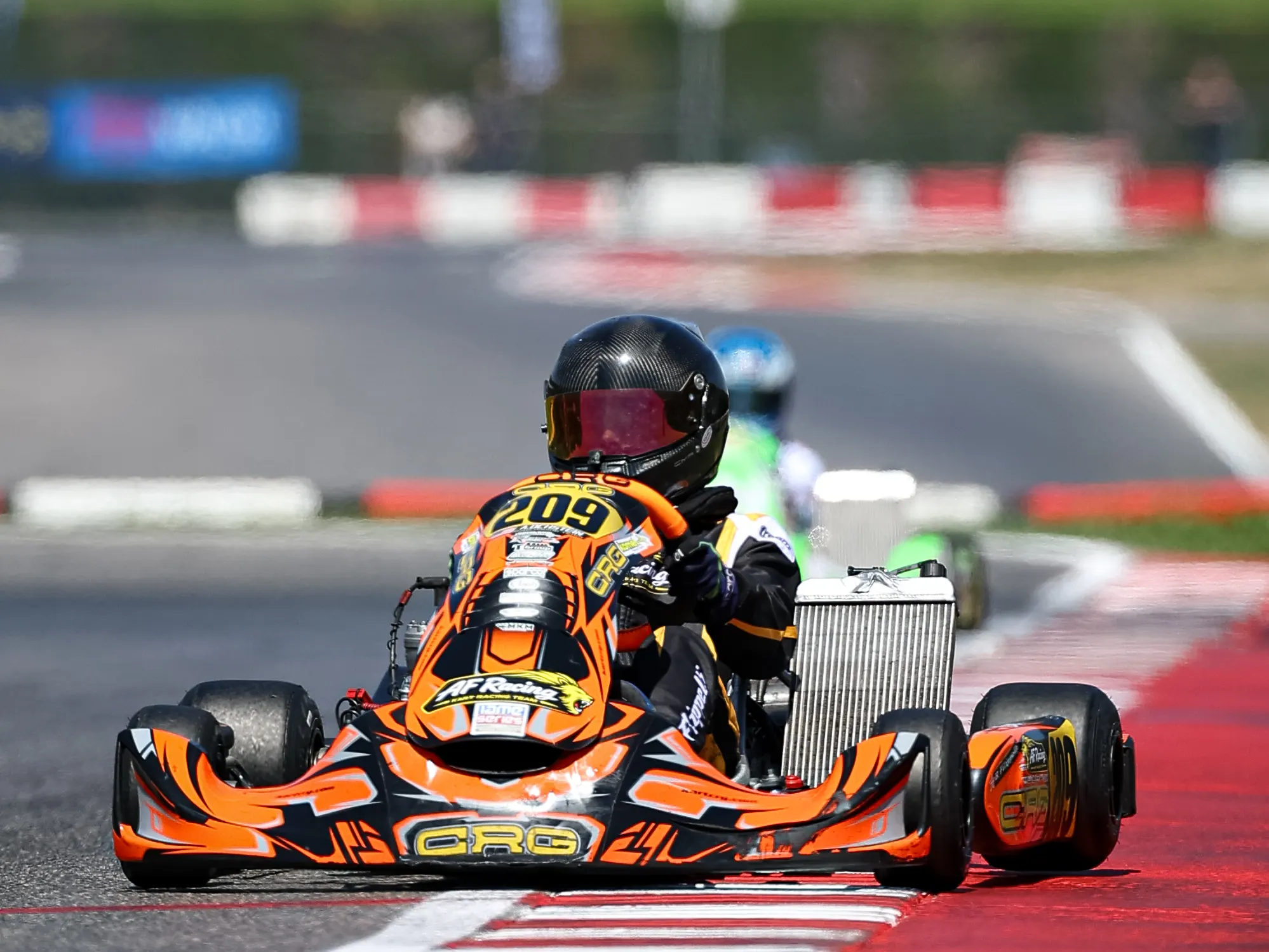 Kart arancione in uscita di curva sul cordolo rosso
