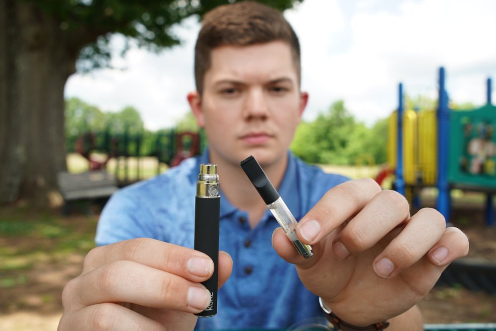 Jay Jenkins holds a Yolo! brand CBD oil vape cartridge alongside a vape pen at a park in Ninety Six, S.C., on Wednesday, May 8, 2019. (AP Photo/Allen G. Breed)