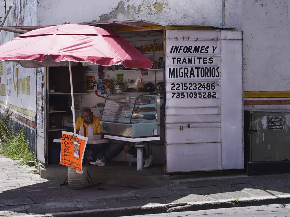 Un anuncio con información para el que busque ayuda en sus trámites migratorios está pintado en un puesto de un vendedor de empanadas situado frente a la oficina principal de inmigración en Puebla, México, el 23 de septiembre de 2022. Con el creciente número de migrantes que entran en México, se ha multiplicado una extensa red de abogados e intermediarios dispuestos gestionar las necesidades de los migrantes. (AP Foto/Marco Ugarte)