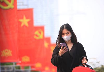 Fotografía de archivo del 23 de enero de 2021 de una mujer con mascarilla viendo su teléfono en Hanoi, Vietnam. (AP Foto/Hau Dinh, Archivo)