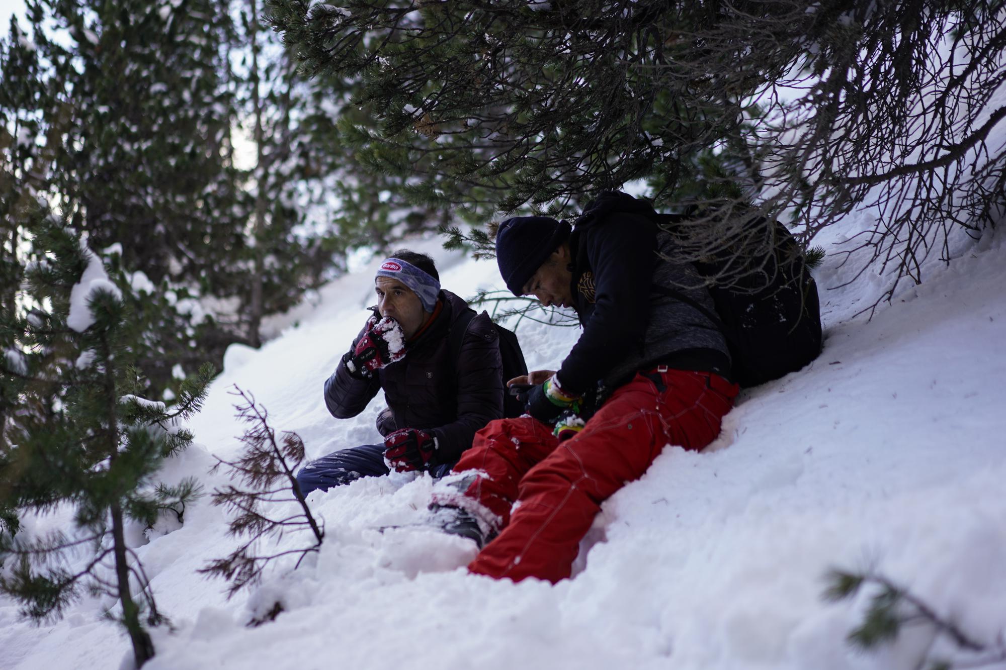 Afghan migrant Sayed Hamza, left, eats snow during a trek across the French-Italian Alps to reach a migrant refuge in Briancon, France, Sunday, Dec. 12, 2021. (AP Photo/Daniel Cole)