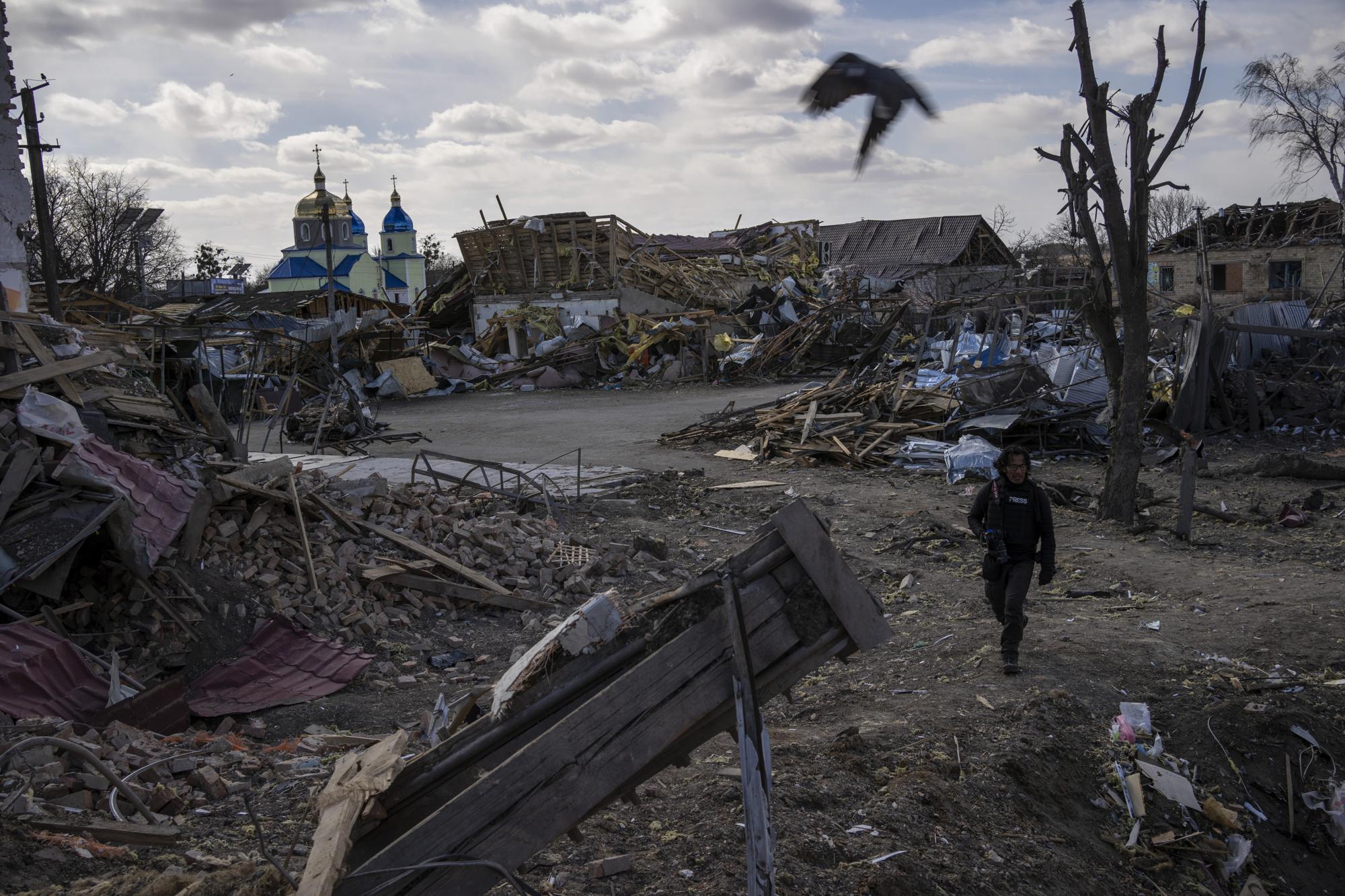 A journalist walks amid the destruction after a Russian attack in Byshiv on the outskirts of Kyiv, Ukraine, Sunday, March 27, 2022. (AP Photo/Rodrigo Abd)
