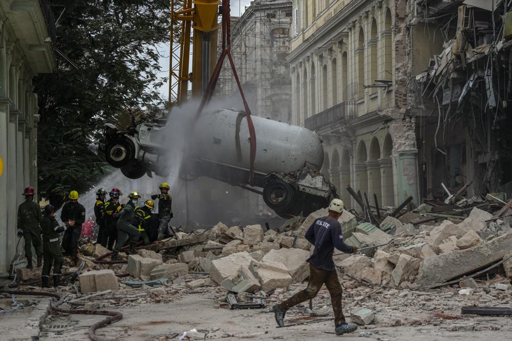 Los bomberos rocían con agua un camión cisterna para enfriarlo mientras lo retiran del lugar de una explosión mortal que destruyó el Hotel Saratoga de cinco estrellas, en La Habana, Cuba, el viernes 6 de mayo de 2022. Una poderosa explosión aparentemente causó por una fuga de gas natural mató al menos a 18 personas, incluida una mujer embarazada y un niño, e hirió a decenas el viernes cuando voló las paredes exteriores del hotel de lujo en el corazón de la capital de Cuba.  (Foto AP/Ramón Espinosa)n Espinosa)
