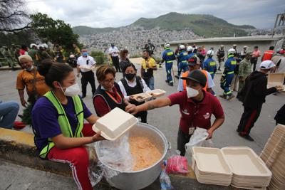 Voluntarios sirven platos de comida para personas que participan en las tareas de búsqueda y rescate en el lugar donde se registró el desprendimiento de rocas gigantescas que cayeron sobre una zona habitacional, en Tlalnepantla, en las afueras de Ciudad de México, el sábado 11 de septiembre de 2021. (AP Foto/Ginnette Riquelme)