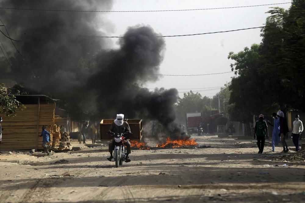 A man ride a bike past fire following a protest in N'Djamena, Chad, Tuesday, April 27, 2021. Thousands of people protested and two people were killed in Chad Tuesday in demonstrations against the rule of a transitional military council headed by the son of the late President Idriss Deby Itno, who was killed last week. (AP Photo/Sunday Alamba)