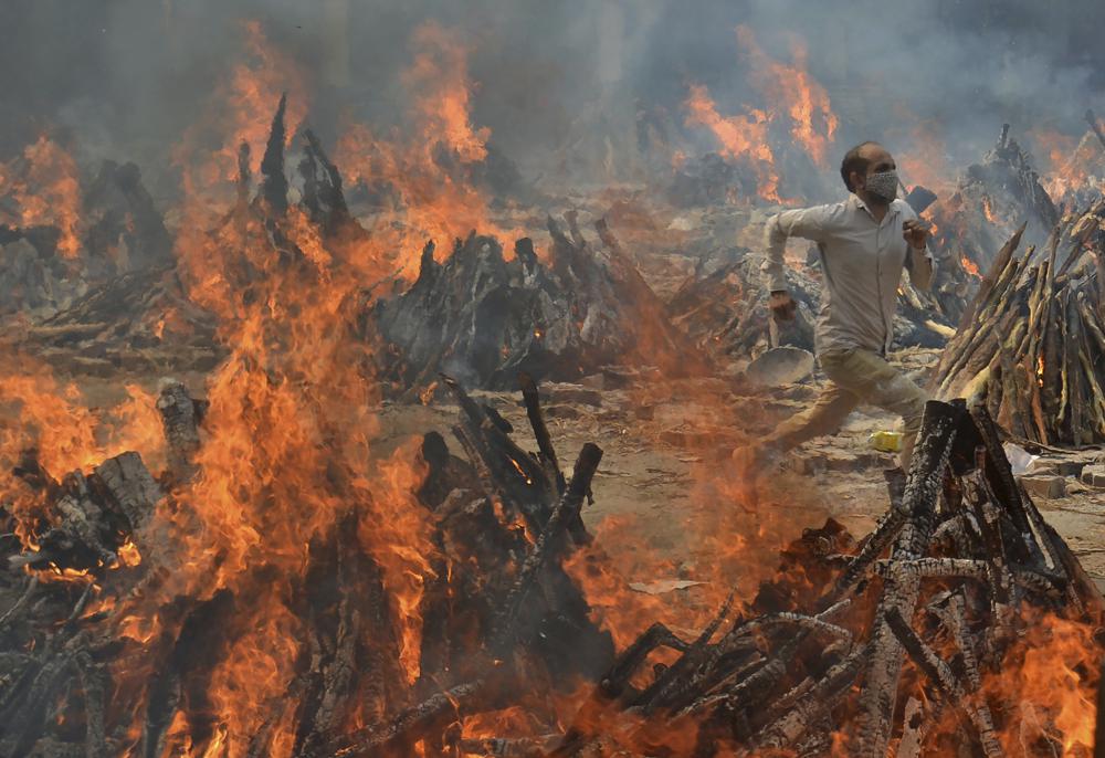 FILE - In this April 29, 2021, file photo, a man runs to escape heat emitting from the multiple funeral pyres of COVID-19 victims at a crematorium in the outskirts of New Delhi, India. Indias excess deaths during the pandemic could be a staggering 10 times the official COVID-19 toll, likely making it modern Indias worst human tragedy, according to the most comprehensive research yet on the ravages of the virus in the south Asian country. (AP Photo/Amit Sharma, File) qeithiediqxxkmp