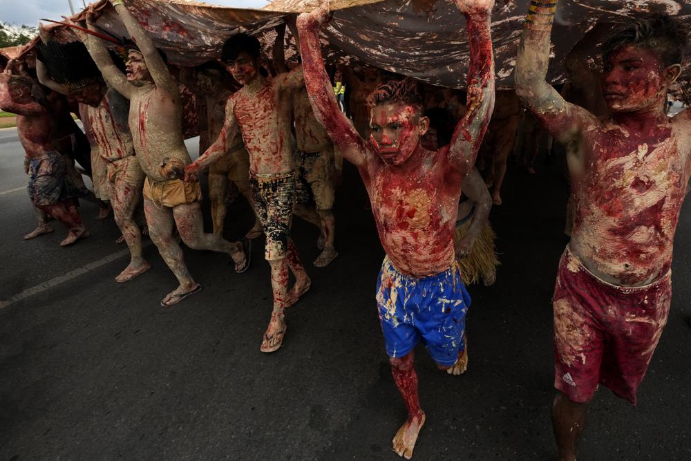 FILE - Indigenous people painted with red ink representing spilled Indigenous blood and clay representing gold, march during a protest against the increase of mining activities that are encroaching on their land, in front of the Ministry of Mines and Energy, in Brasilia, Brazil, Monday, April 11, 2022. (AP Photo/Eraldo Peres, File)