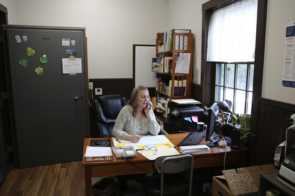 Victory Town Clerk Tracey Martel takes a phone call at the town clerk's office, in Victory, Vt., Thursday March 31, 2022. Martel says she's regularly frustrated watching a spinning circle on her computer while she tries to complete even the most basic municipal chores online. It could be years before high-speed internet reaches Victory. The need to connect homes and businesses to high-speed broadband services was highlighted by the COVID-19 pandemic and officials say that while there is lots of money available, supply and labor shortages are making the expansion a challenge. (AP Photo/Wilson Ring)