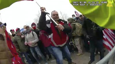 Esta toma de una cámara corporal del Departamento Metropolitano de Policía muestra a Thomas Webster, un exinfante de Marina que viste chaqueta roja, el 6 de enero de 2021 frente a una barricada policial del lado oeste del Capitolio de Estados Unidos, en Washington. (Departamento Metropolitano de Policía vía AP)