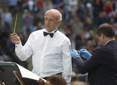 El director Ivan Fischer, fundador de la Orquesta del Festival de Budapest, recibe su tercera dosis de la vacuna contra el COVID-19 mientras dirige a la orquesta en un concierto gratuito al aire libre en Budapest, Hungría, el miércoles 25 de agosto de 2021. (AP Foto/Laszlo Balogh)