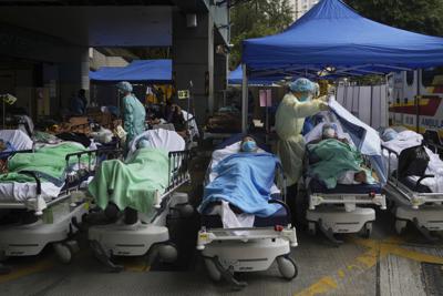 Pacientes esperan en camas de hospital por una plaza en un centro médico improvisado en el exterior del centro Caritas, en Hong Kong, el 18 de febrero de 2022. (AP Foto/Kin Cheung)