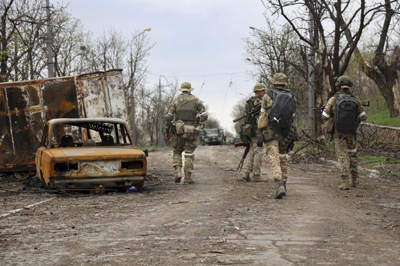 Servicemen of Donetsk People's Republic militia walk past damaged vehicles during a heavy fighting in an area controlled by Russian-backed separatist forces in Mariupol, Ukraine, Tuesday, April 19, 2022. Taking Mariupol would deprive Ukraine of a vital port and complete a land bridge between Russia and the Crimean Peninsula, seized from Ukraine from 2014. (AP Photo/Alexei Alexandrov)