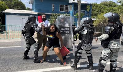 Una migrante es detenida por efectivos de la Guardia Nacional que impiden a algunos migrantes salir de Tapachula, México, mientras otros pasan corriendo, el viernes 1 de abril de 2022. (AP Foto/Edgar H. Clemente)