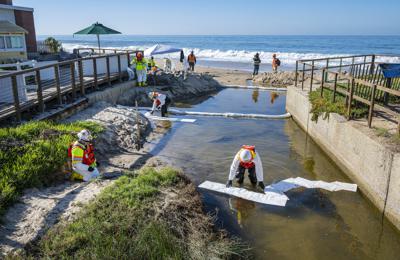 Equipos de limpieza utilizan material absorbente para retirar petróleo que pudiera haber ingresado a un pequeño riachuelo que desemboca en el océano, luego de una fuga en un oleoducto, el jueves 14 de octubre de 2021, en Laguna Beach, California. (Mark Rightmire/The Orange County Register vía AP)