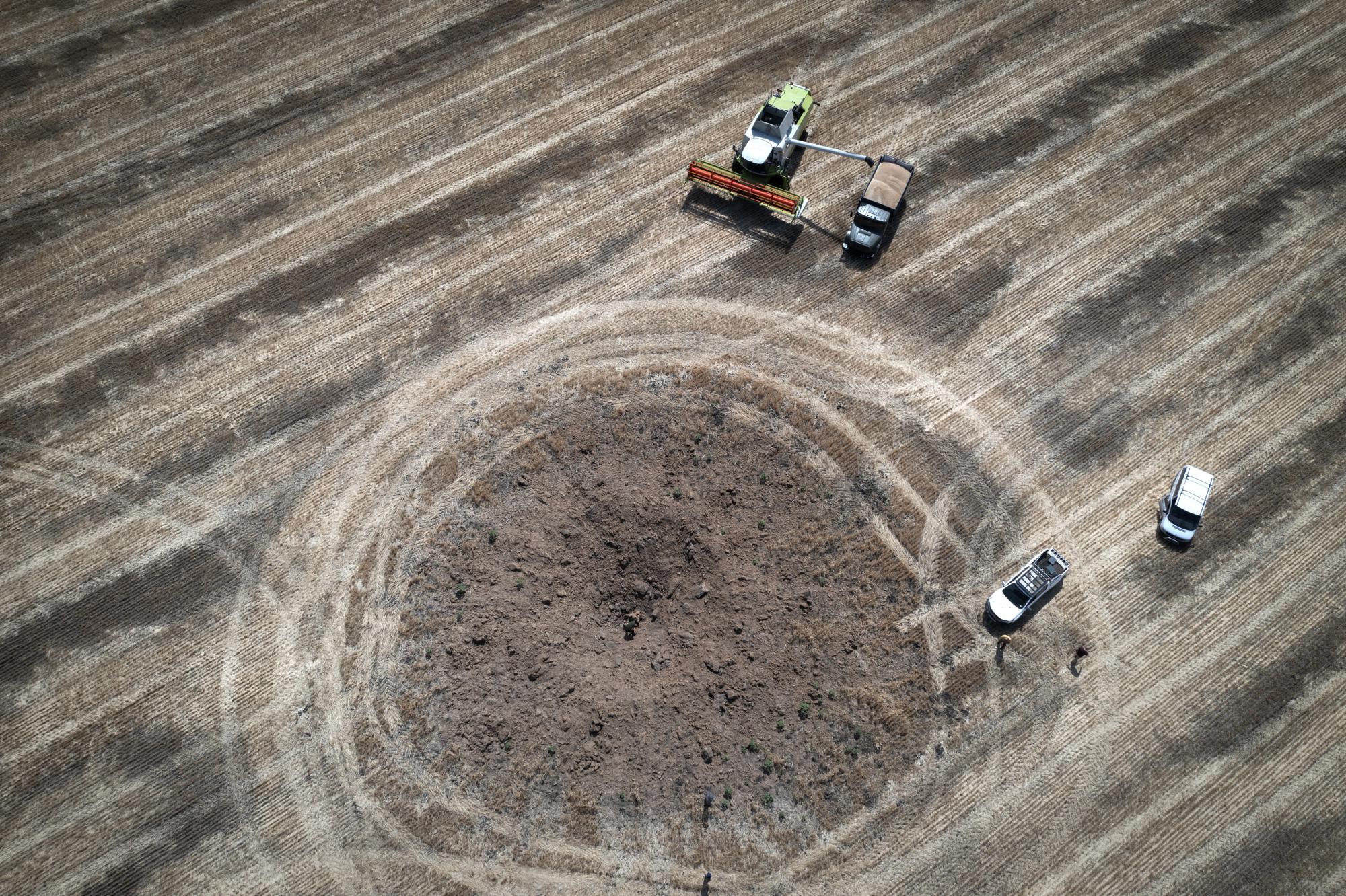 FILE - Next to a crater left by a Russian rocket, a farmer harvests a field 10 kilometers (6 miles) from the front line between Russian and Ukranian forces, in the Dnipropetrovsk region, Ukraine, Monday, July 4, 2022. (AP Photo/Efrem Lukatsky, File)