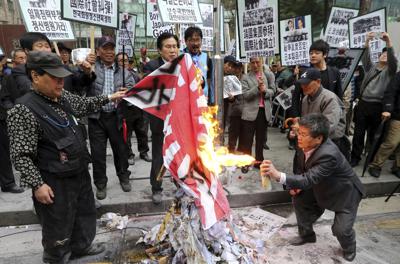 ARCHIVO - En esta foto de archivo del 25 de abril de 2015, miembros de organizaciones conservadoras surcoreanas queman una bandera japonesa del sol naciente durante una protesta en Seúl (Lee Jung-hoon/Yonhap via AP, archivo)