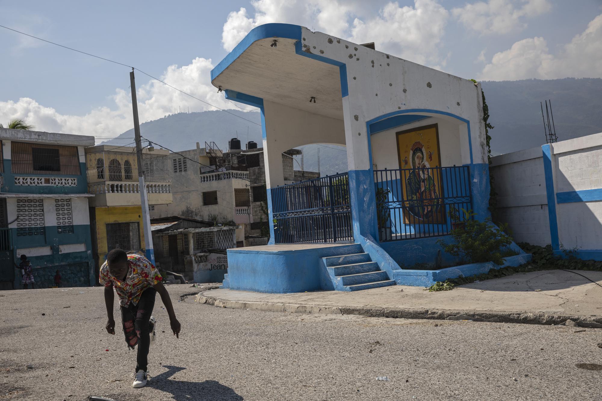 A man runs for cover as he crosses a barricaded street in the gang-controlled Bel Air neighborhood of Port-au-Prince, Haiti, Saturday, Sept. 25, 2021. More than a city, Port-au-Prince is an archipelago of gang-controlled islands. Some neighborhoods are abandoned. Others are barricaded behind fires, destroyed cars and piles of garbage, occupied by heavily armed men. (AP Photo/Rodrigo Abd)