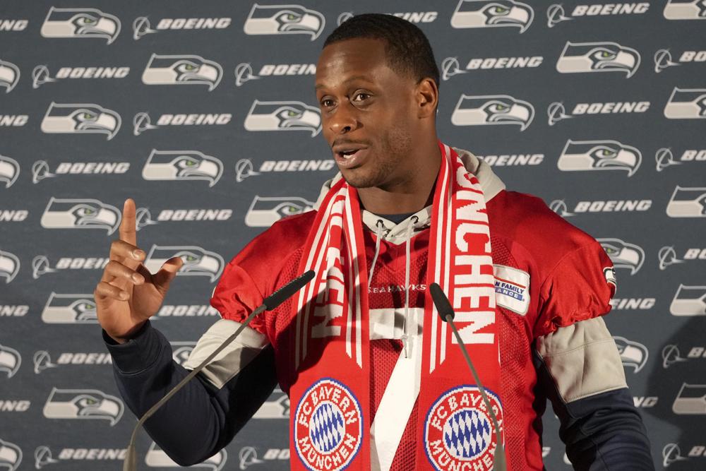 El mariscal de campo de los Seattle Seahawks, Gino Smith, usa una bufanda del Bayern Munich FC mientras responde preguntas durante una conferencia de prensa después de una sesión de práctica en Munich, Alemania, el jueves 10 de noviembre de 2022. Los Tampa Bay Buccaneers están programados para jugar el juego de los Seattle Seahawks de la NFL en el Allianz Arena en Munich el domingo.  (Foto AP/Matthias Schrader)