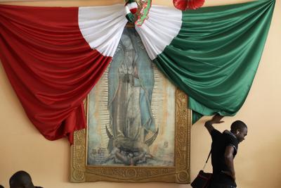 Con una imagen de la Virgen María y la bandera de México de fondo, un haitiano escucha música mientras espera una cama en el refugio para migrantes Padre Chava, en Tijuana, México, el 26 de septiembre de 2016. (AP Foto/Gregory Bull)