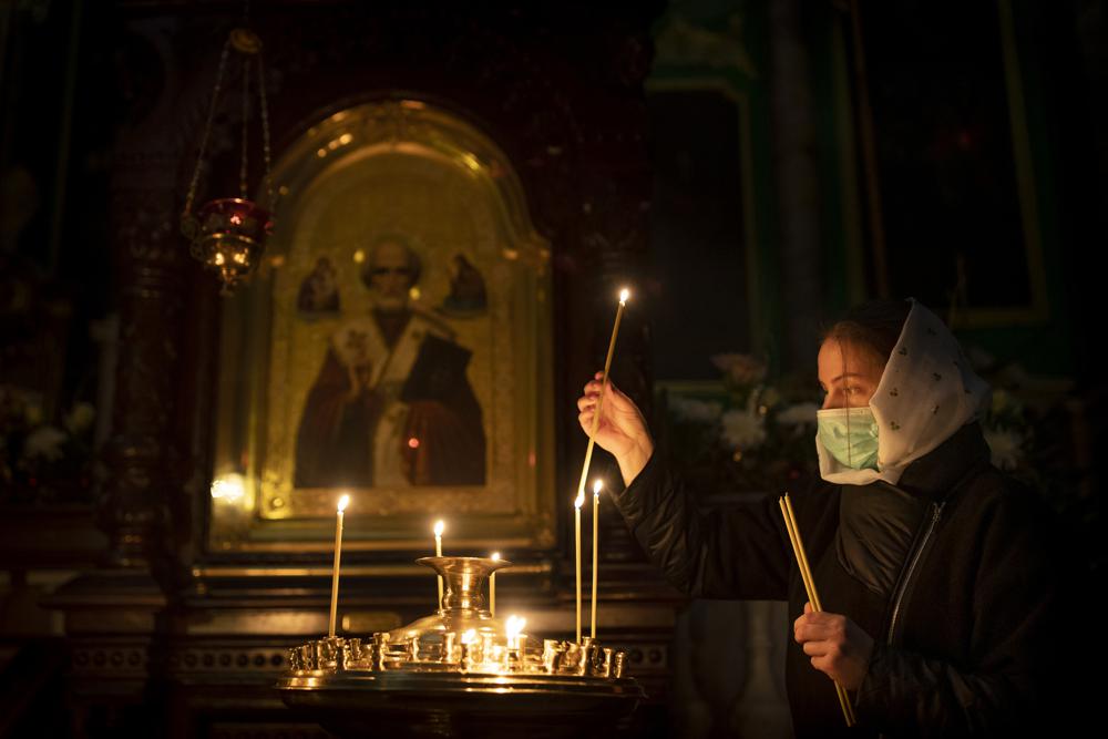 A Lithuanian Orthodox believer wearing a face mask to prevent the spread of the coronavirus, lights candles before the liturgy on Orthodox Christmas Eve in the Orthodox Church of the Holy Spirit in Vilnius, Lithuania, Thursday, Jan. 6, 2022. (AP Photo/Mindaugas Kulbis)