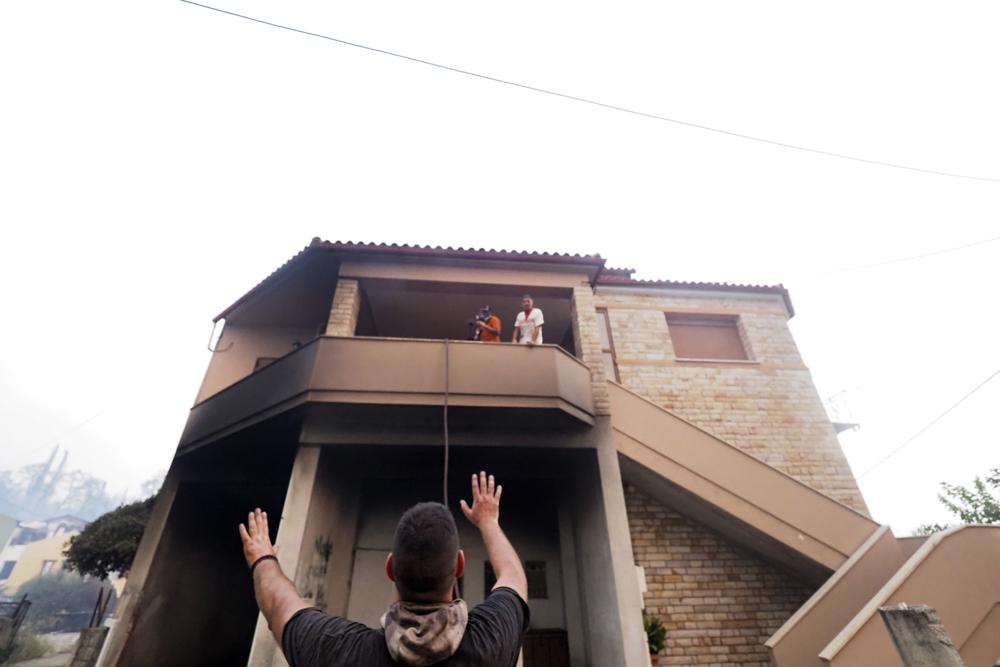 People try to extinguish a fire at a house in Rovies village on the island of Evia, about 160 kilometers (100 miles) north of Athens, Greece, Wednesday, Aug. 4, 2021. Greece evacuated people in boats from an island beach Wednesday amid heavy smoke from a nearby wildfire and fire crews fought elsewhere to keep flames away from the birthplace of the ancient Olympic Games as the country sweltered under a record heat wave. (AP Photo/Thodoris Nikolaou)